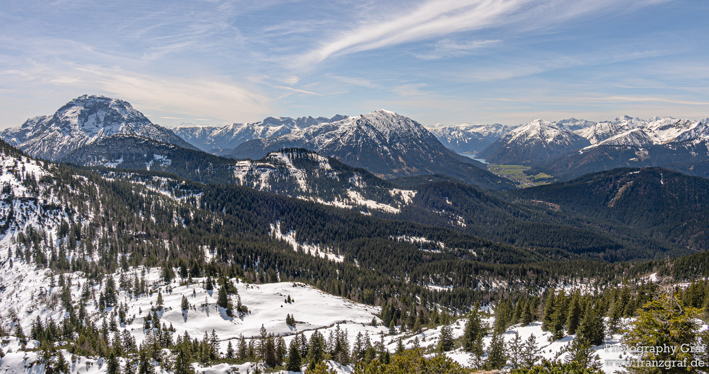 This image captures a breathtaking view of a snowy mountain range, enveloped in a serene atmosphere. The foreground is adorned with a variety of trees, their branches heavy with snow, illustrating the depth of winter. The mountains themselves rise majestically, their peaks and ridges covered in a pristine white blanket, hinting at the harsh yet beautiful conditions. Above, the sky is a canvas of soft clouds, suggesting a calm weather. The presence of elements such as glacial landforms and possibly moraines indicates the geological richness of the area, while the mention of larch trees adds a botanical interest, hinting at the specific flora adapting to these cold climates. The overall scene evokes a sense of wilderness and untouched nature, inviting viewers to contemplate the quiet beauty of winter landscapes.